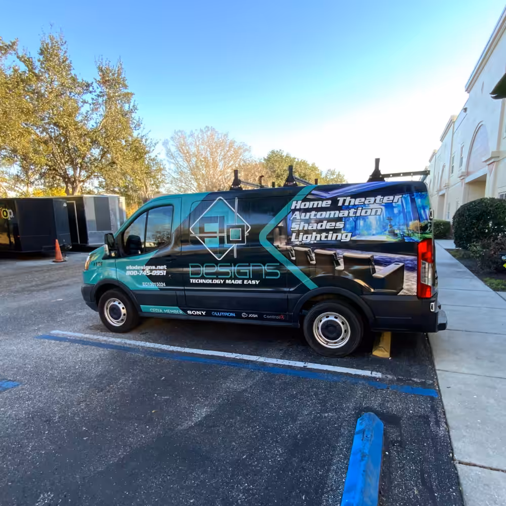 A van branded with Designs and technology services, featuring fleet wraps Sarasota, is parked in a lot near trees and a building. The tech-themed graphics showcase expertise from the Sarasota Sign Shop.