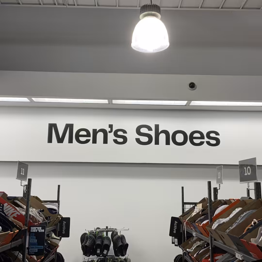 A retail store aisle sign reads Mens Shoes above shelves filled with various styles of mens footwear.