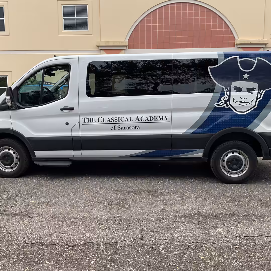 A white van with The Classical Academy of Sarasota logo and a large patriot head, representing Schools & Sports, is parked in front of a beige and pink building.