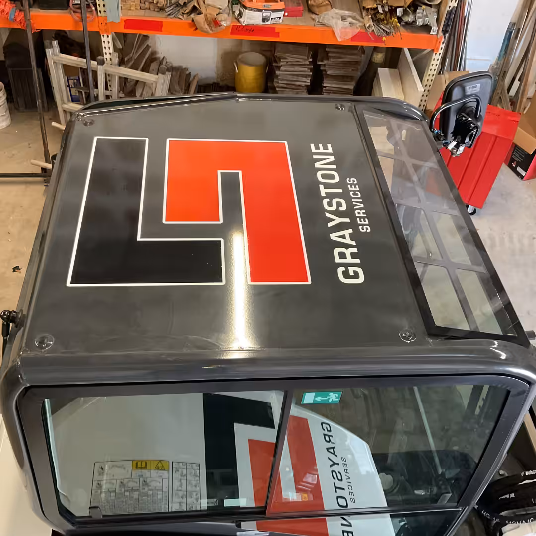 View from above of a Home Service vehicle with a large L7 logo and GRAYSTONE SERVICES text on the roof, parked inside a cluttered workshop with tools and equipment visible on shelves.