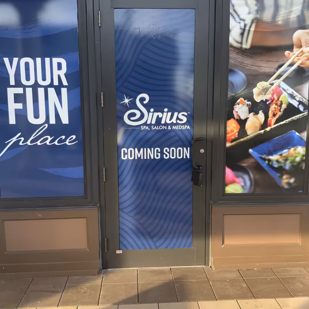 A storefront door displays a sign for Sirius Spa, Salon & Medspa Coming Soon. Nearby retail windows show sushi in chopsticks and the words YOUR FUN place on a blue background.