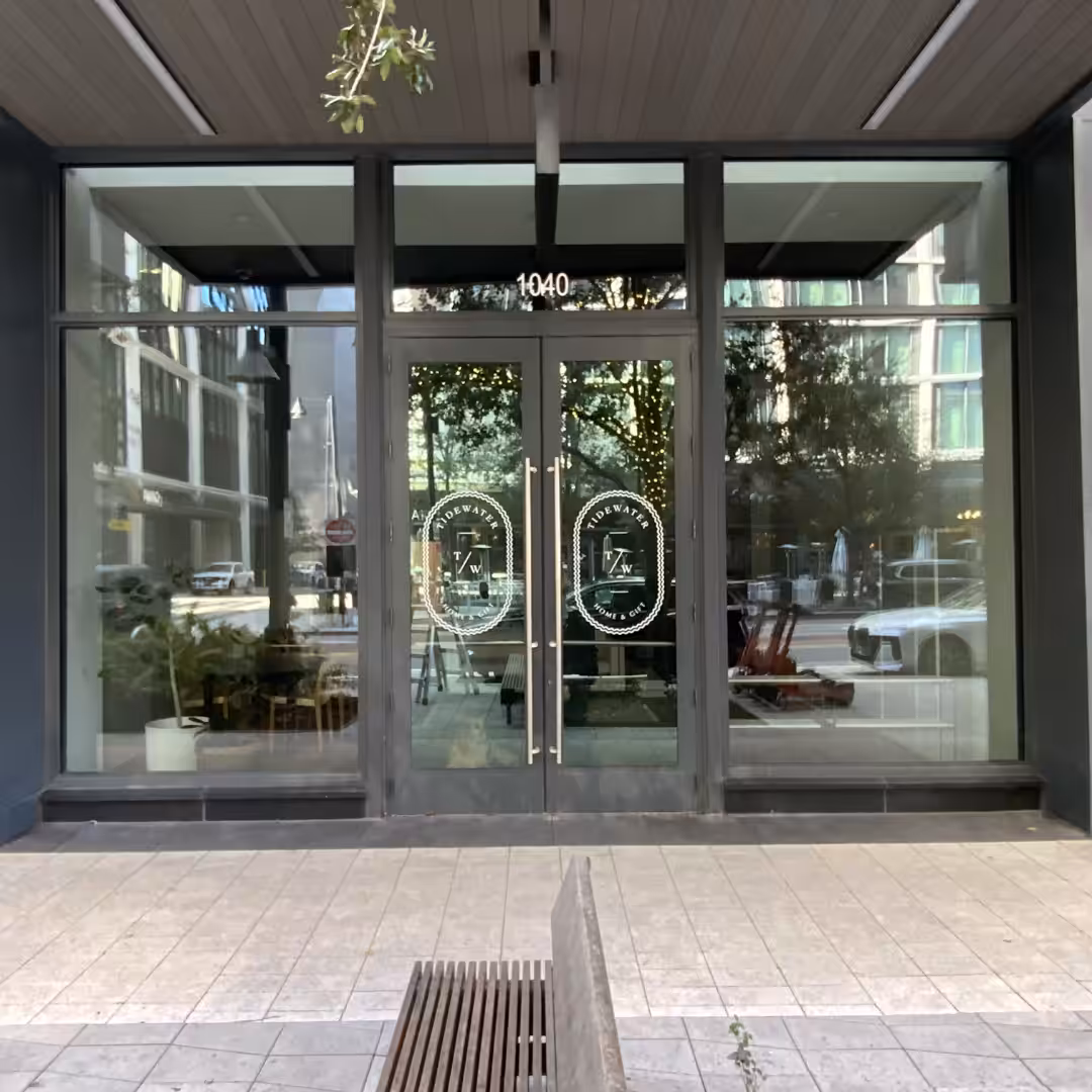 Glass storefront retail doors with Together We Brew and a coffee cup logo; reflections of city buildings and trees are visible. The entrance is at 1040, with plants, seats inside, and a wooden bench outside the door.