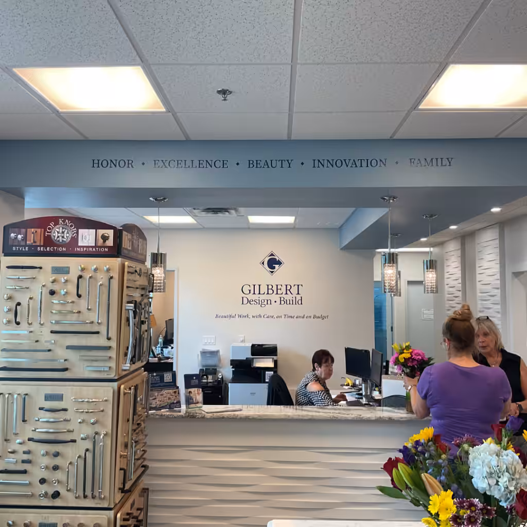 Reception area of a design business with employees at the desk, floral arrangements in the foreground, indoor business signs, and cabinet hardware displays. Words like HONOR and FAMILY are written on the wall above the desk.